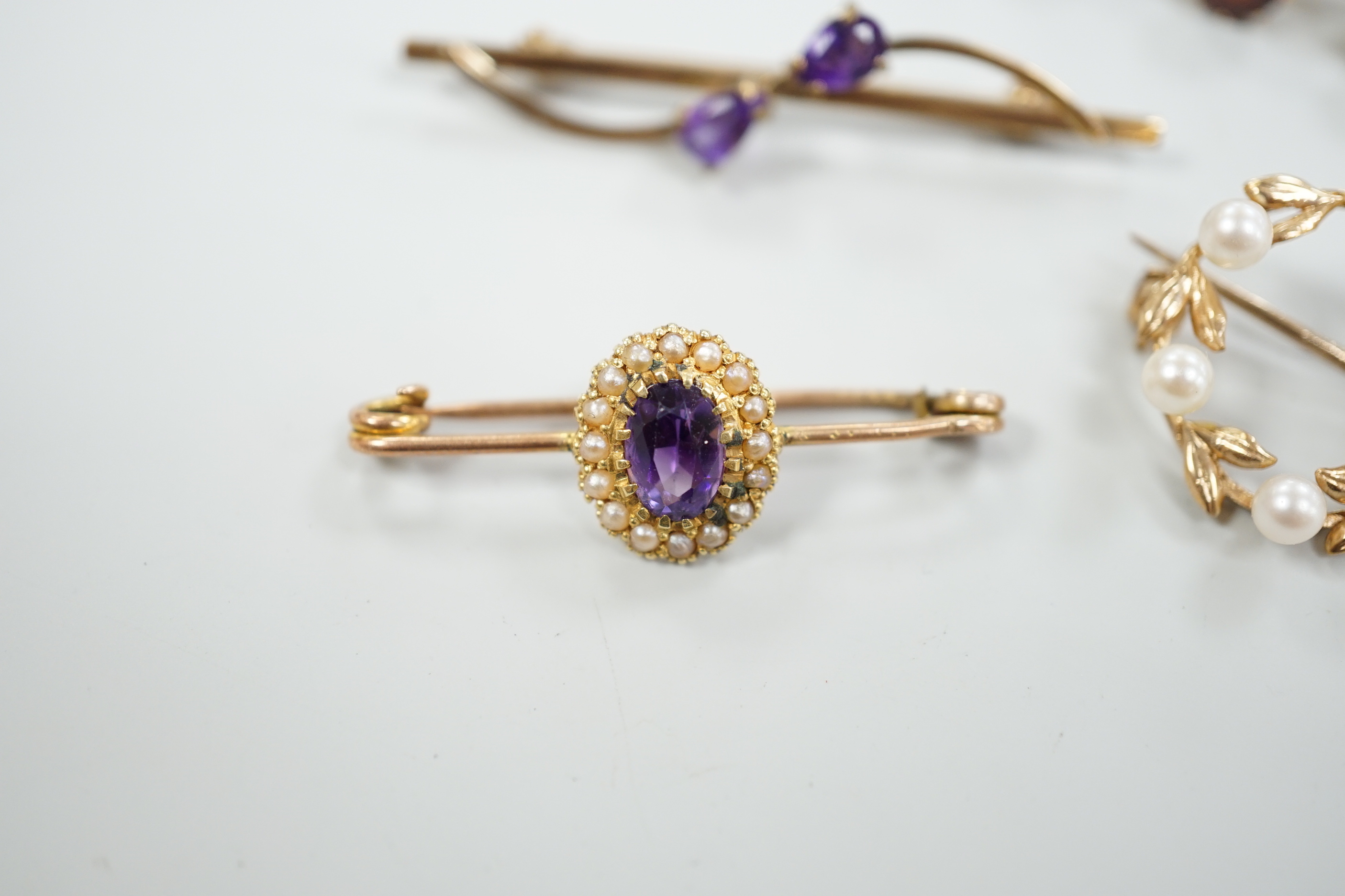 A 15ct and graduated five stone garnet set bar brooch, 48mm, a similar amethyst and seed pearl cluster set brooch and two other gem set brooches, including 9ct gold.